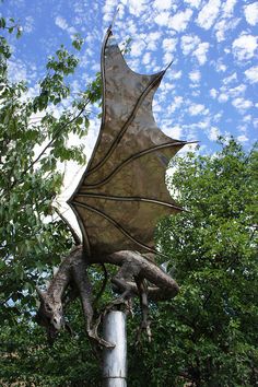 a statue of a dragon on top of a pole with trees in the back ground