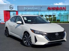 a white car is parked in front of a nissan dealership with the brand's logo on it