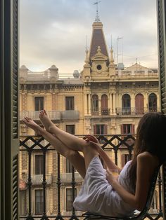 a woman sitting in a chair on top of a balcony next to a tall building