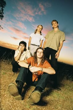 four people sitting on the ground in front of a sunset