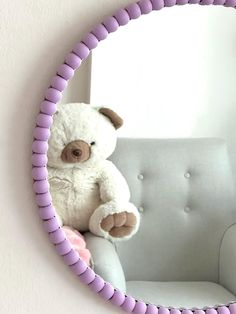 a white teddy bear sitting on top of a chair in front of a round mirror