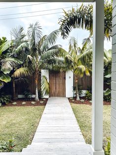 a wooden walkway leading to a white door surrounded by palm trees