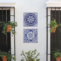 two blue and white tiles are on the wall next to potted plants