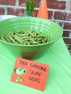 a green bowl filled with peas next to a sign that says pea shooter snap peas