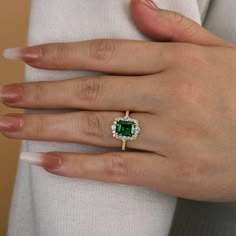 a woman's hand wearing a ring with an emerald and white diamond center stone