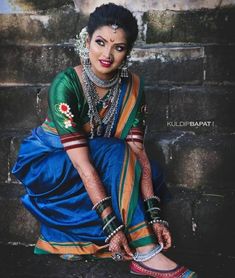 a woman sitting on the ground in a blue and green sari with jewelry around her neck