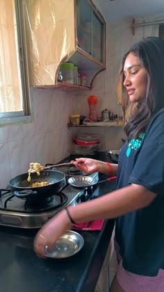 a woman standing in front of a stove cooking food on top of a pan with a spatula