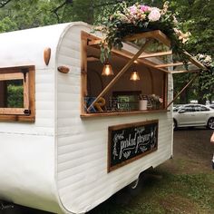 a small white trailer parked next to a forest filled with lots of trees and flowers