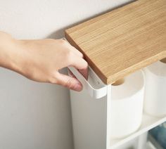 a person's hand is holding the door handle on a shelf with two rolls of toilet paper