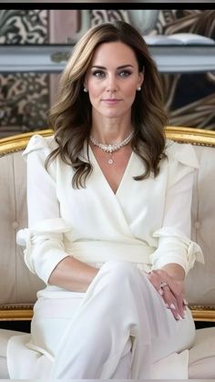 a woman sitting on top of a couch wearing a white suit and diamond choker