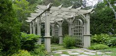 an outdoor garden with stone walkway and pergolated arbor, surrounded by greenery