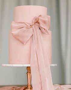 a pink wedding cake with a large bow on the top and ribbon tied around it