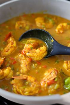 a pot filled with shrimp and vegetables being stirred by a ladle on the stove