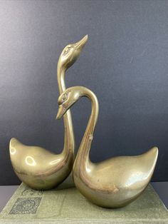 two brass swan sculptures sitting on top of a green bookcase next to each other