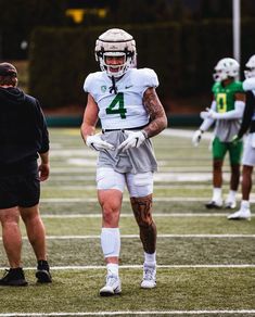 a football player walking on the field with his hands in his pockets while wearing white and green uniforms