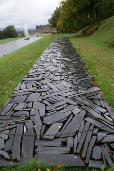 a long path made out of rocks in the middle of a grassy area next to a body of water