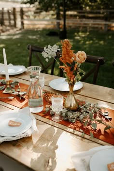 a wooden table topped with white plates and flowers