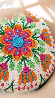 a crocheted round pillow with colorful flowers on it sitting on a white surface