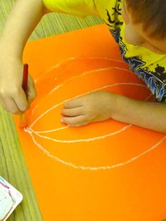 a young boy drawing on an orange piece of paper