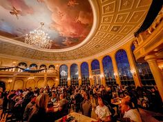 a restaurant filled with lots of people sitting at tables and eating food in front of a painting on the ceiling