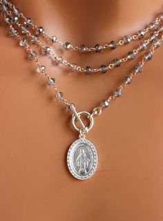 "This a a beautiful triple layer crystal bead necklace with Mary's miraculous medal hanging from toggle front. These lovely layers are made of 4mm grey rondelle crystals on sterling silver chain. This medium size Mother Mary pendant is sterling silver with pave crystals, measuring 22x15mm, hanging form the sterling silver toggle. This necklace is 925 sterling silver. This necklace can be worn many ways as shown in photos. Comes in a 50\" length. All my jewelry comes in a cute gift box with jewel Catholic Jewelry Necklace, Multi Strand Necklaces, Cross Pendant Necklace Woman, 14kt Gold Jewelry, Miraculous Medal Necklace, Cross Choker, Clean Sterling Silver, Crystal Bead Necklace, Miraculous Medal