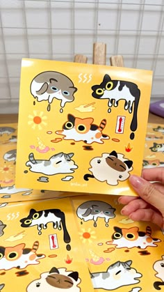 a person holding up some stickers on top of a yellow table with cats and dogs