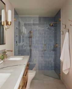 a bathroom with blue tile and gold fixtures on the shower wall, along with two sinks