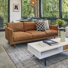 a living room with couches, tables and chairs in front of large windows that look out onto the woods