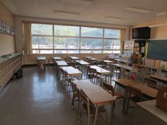 an empty classroom with desks and chalkboards on the wall in front of large windows