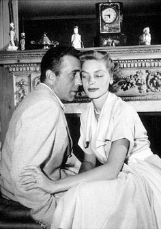 a black and white photo of a man and woman sitting next to each other in front of a fireplace