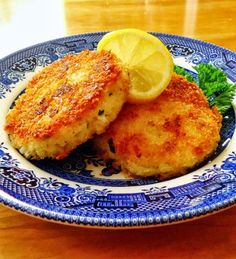 two crab cakes on a blue and white plate with lemon wedges next to it