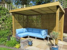 a blue couch sitting in the middle of a garden next to a wooden pergolan