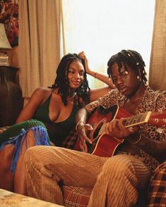 two people sitting on a couch playing guitar and one is wearing a leopard print shirt