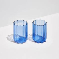 two blue glass vases sitting on top of a white table next to each other