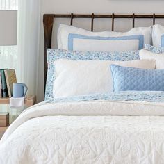 a bed with blue and white comforters in a bedroom next to a nightstand on a wooden headboard