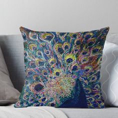 a colorful peacock throw pillow sitting on top of a couch with its feathers spread out