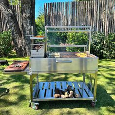 an outdoor grill is set up in the grass with food on it and cooking utensils