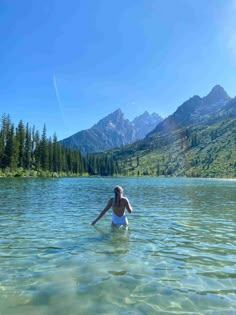 a woman wading in the water near mountains