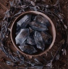 a wooden bowl filled with ice cubes on top of a wood table next to dried plants