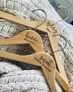 three wooden hangers with names on them sitting on a white knitted blanket,