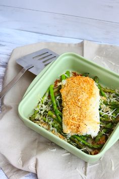 a green dish with fish and asparagus on it, next to a fork