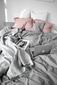 an apple laptop sitting on top of a bed covered in blankets and pillows with pink pillows