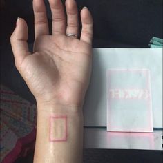 a person's hand with a small square tattoo on their left wrist, next to an envelope