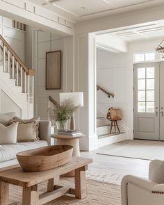 a living room filled with furniture and a wooden table next to a stair case in front of a white door