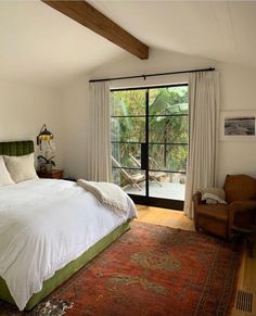 a bedroom with a bed, chair and large window looking out onto the yard outside