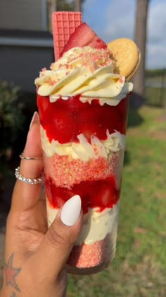 a person holding up an ice cream sundae with strawberries and whip cream on top