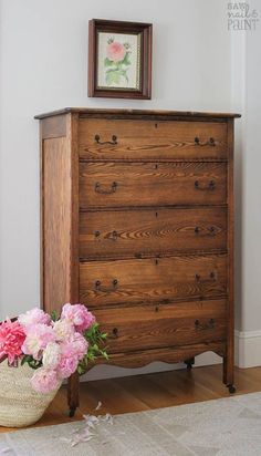 a wooden dresser sitting next to a basket with flowers in it on top of a hard wood floor