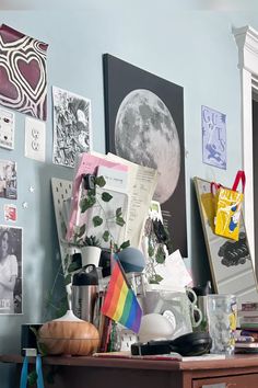 a cluttered desk with various items on it in front of a wall full of pictures