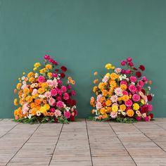 two vases filled with colorful flowers sitting on top of a tiled floor next to a green wall