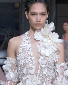 a model walks down the runway in a white dress with flowers on it's shoulders